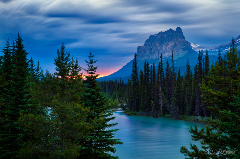 Castle Mountain in Banff National Park at dusk with the Bow river in the foreground.