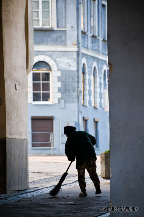An elderly woman sweeps the road leading through the Gates of Dawn in Vilnius.