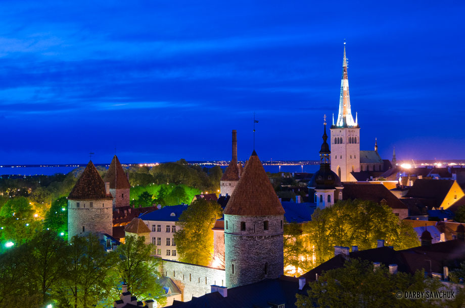 Tallinn's city walls and St. Olav's Church in the background at night.