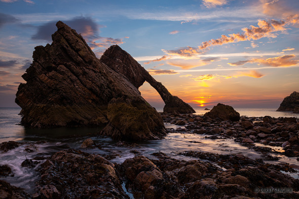 The sun rises behind Bow Fiddle Rock off the north Coast of Aberdeenshire, Scotland.