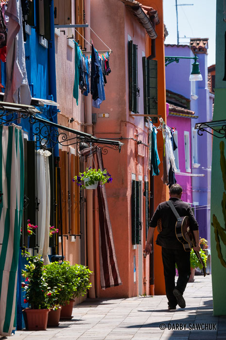A guitarist walks down one of the brightly coloured alleys in Burano, Italy.