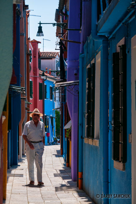 A man walks down a narrow, colourful alley in Burano, Italy.