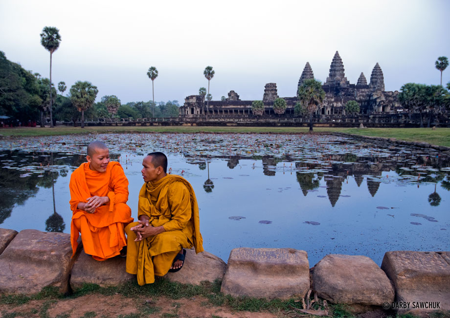 Novice Buddhist monks chat near one of the ponds in front of the central structure of Angkor Wat temple in Cambodia.