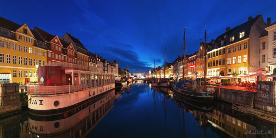 The blue sky of dusk reflects in a panoramic image of the still waters of the Nyhavn Canal in Copenhagen, Denmark.