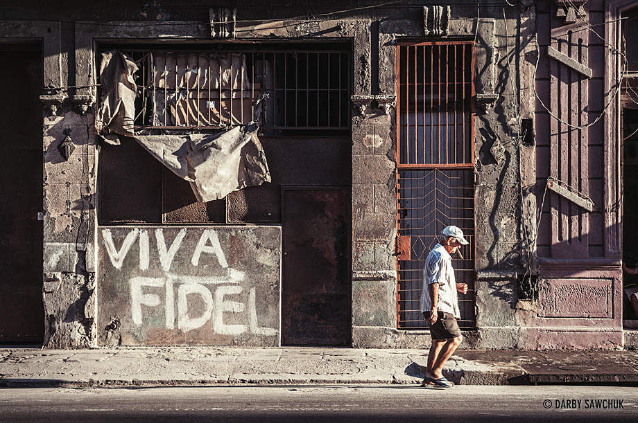 A cuban man smokes a cigar and walks past graffiti reading 'Viva Fidel' in reference to the country's former leader, Fidel Castro.