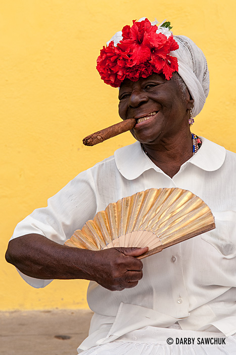 A cigar-smoking woman poses with a fan in Havana, Cuba.