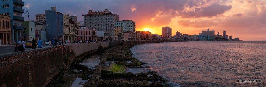 A panoramic view of the sun setting over the Malecon sea wall and the Havana skyline.