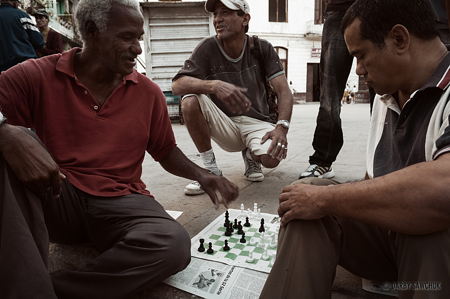 Dominoes, checkers and in this case, chess are widely played out in the open streets in Cuba. Here, men play chess on a simple, paper board in Havana Vieja.