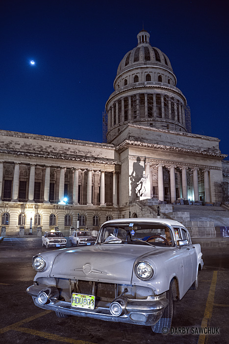 A vintage American car with the National Capitol Building in the background at night.