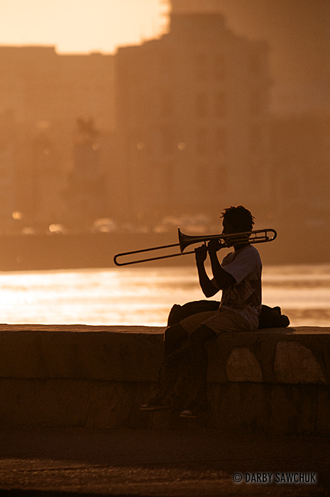 A trombone player practices his instrument on the Malecon sea wall at sunset.