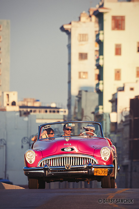 A pink classic convertible taxi carries passengers along one of Havana's wide main roads.