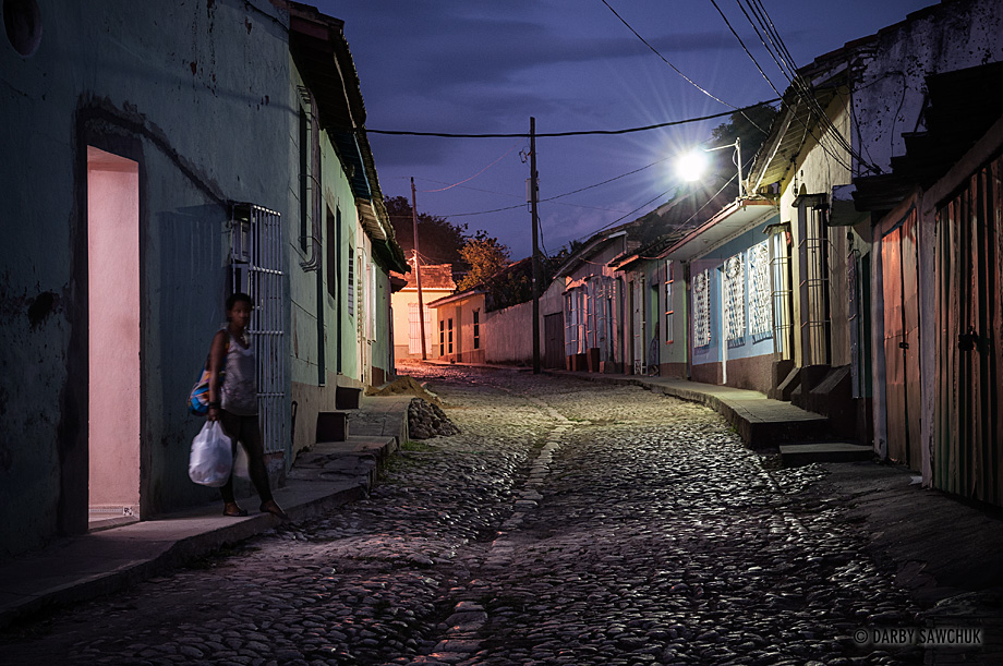 A woman carries groceris through the cobblestoned streets of Trinidad, Cuba at night.