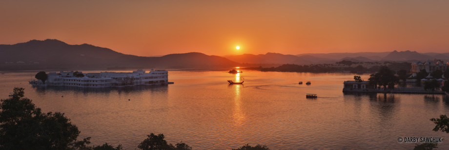 A panoramic image of the sun setting behind Lake Pichola and the Jag Niwas lake palace in Udaipur.