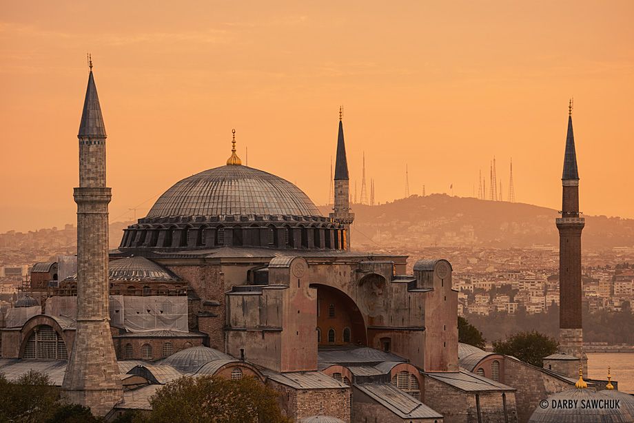 An orange sunrise glow illuminates the Hagia Sophia museum with Camlica Hill in the background.