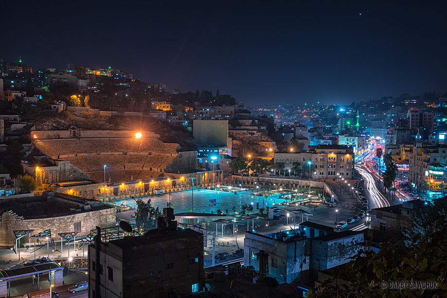 The Roman Theatre and the busy traffic of Amman's surrounding hills at dusk.