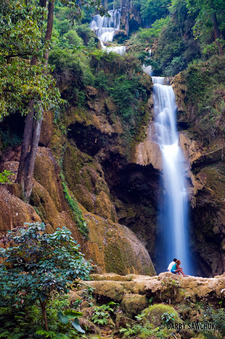 A couple sits in front of the largest cascade at the Kuang Si Falls near Luang Prabang.