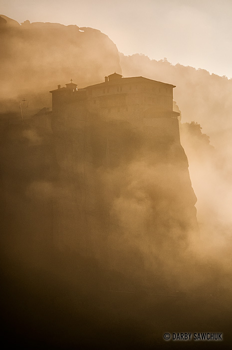 The Monastery of Rousanou is shrouded in mist and clouds at dawn in Meteora, Greece.