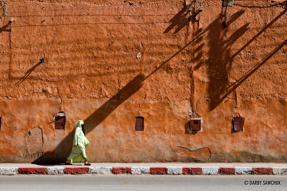 A Moroccan woman walks in front of a highly textured wall in Marrakech.