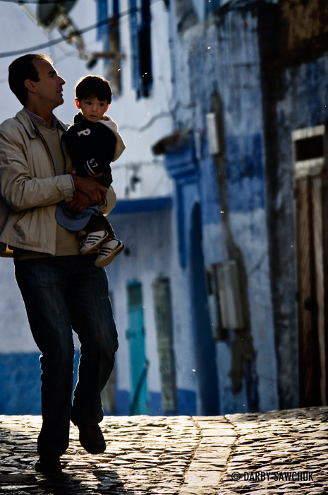 A man carries a child through the streets in Chefchaouen Morocco.