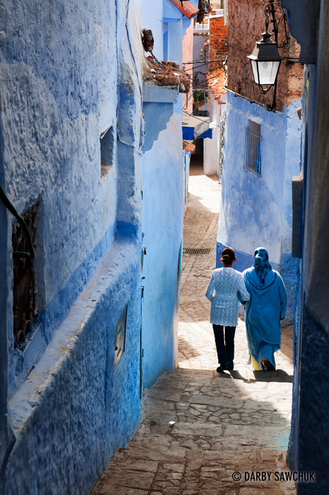 Two women wear blue-coloured clothing that matches the blue-tinted buildings of Chefchaouen.