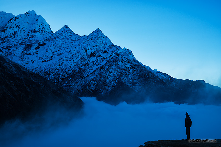 A lone figure watches the clouds roil beneath the Thamserku, one of the Himalayan peaks above Namche Bazaar, Nepal.