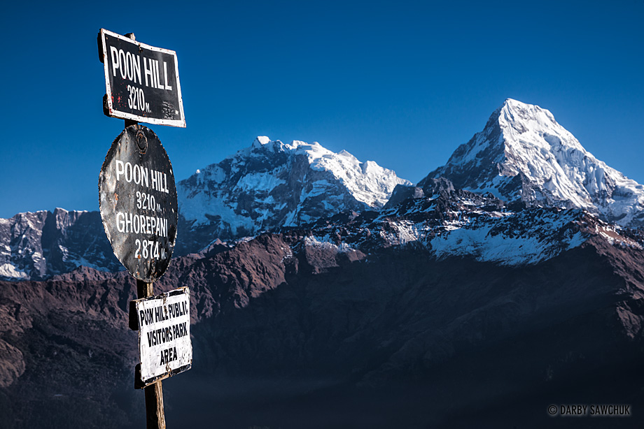 The sign marking the peak of Poon Hill with the Annapurna mountain range in the background.