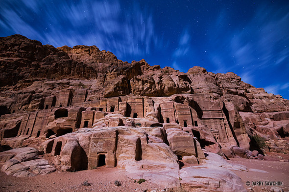 Stars shine through thin clouds over the moonlit Street of Facades at Petra, Jordan.