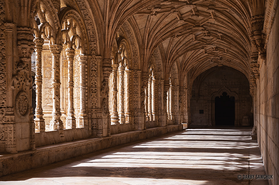 Ornate arches in the Late Gothic Manueline style of architecture are flooded by sunlight in the Jerónimos Monastery in Lisbon.