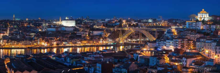 A panoramic image of the Vila Nova de Gaia, Luís I Bridge, and Porto at dusk.