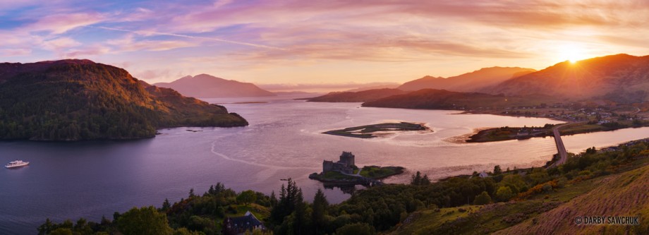 A panoramic photo of the view over Eilean Donan Castle, Luch Duich and Loch Alsh at sunset in Scotland.