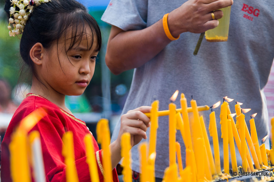 A young girl lights a candle at Phra Singh temple in Chiang Mai, Thailand during Songkran.