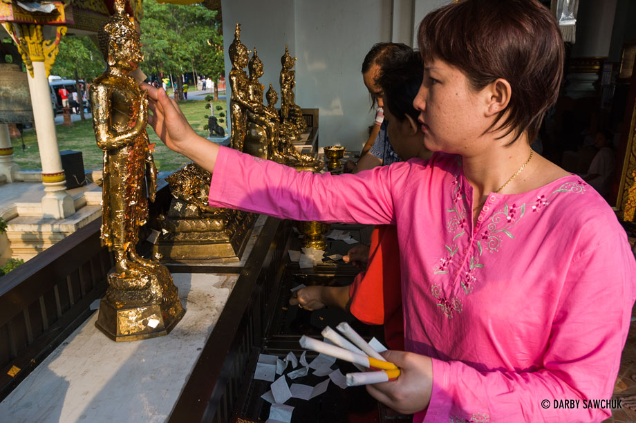A worshipper applies gold leaf to the Buddha images at Wat Phra Singh in Chiang Mai, Thailand during Songkran.