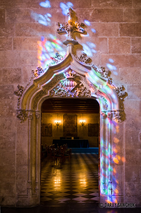 An ornately decorated doorway is bathed in colourful light from a stained glass window in La Lonja in Valencia, Spain.
