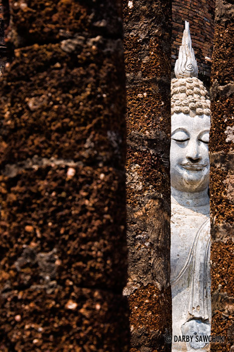 A Buddha statue viewed between ruined pillars at Wat Sa Sri in the Sukhothai Historic Park in Thailand.
