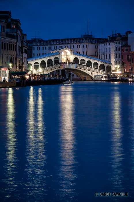 The Rialto Bridge spanning the Grand Canal lit up at dusk in Venice.
