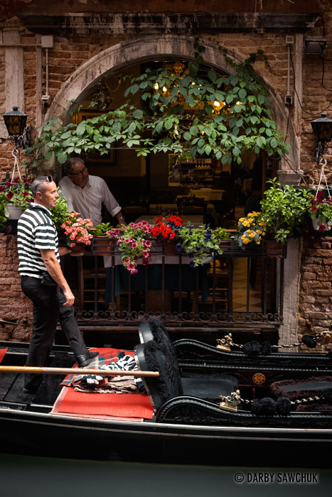 A gondolier talks with a friend at a restaurant open to one of Venice's small canals.