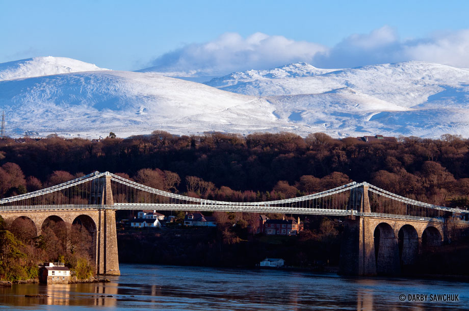 The Menai Suspension Bridge linking the island of Anglesey and the mainland of Wales with the snowy mountains of Snowdonia in the background.