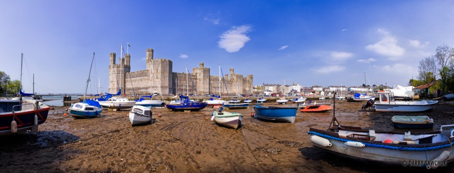 Boats rest at low tide in front of Caernarfon Castle on the river Seiont in Gwynedd, North Wales, UK.