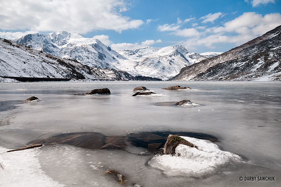 Winter ice covers the surface of Llyn Ogwen looking towards the snow-covered mountains of Snowdonia in North Wales.